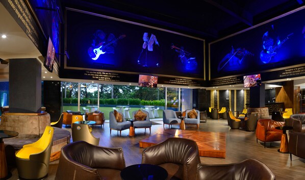 Un espace de détente moderne avec des canapés en cuir, une table basse et un grand écran de télévision diffusant un concert.