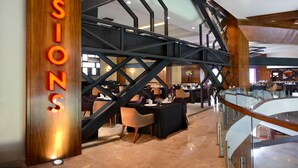 Un interior moderno con un llamativo letrero que dice 'SESSIONS', una barandilla de cristal y una escalera con vigas de madera.