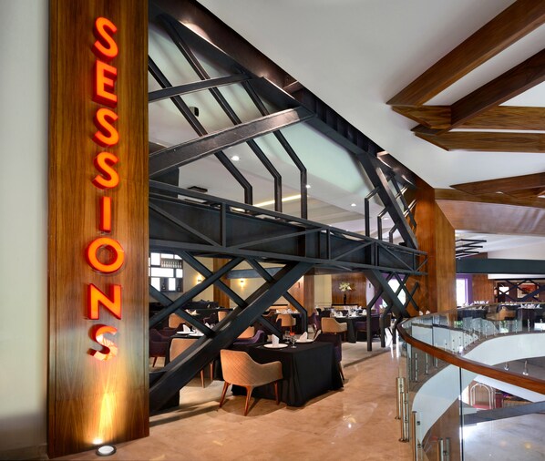 A modern interior with a prominent 'SESSIONS' sign, a glass railing, and a staircase with wooden beams.