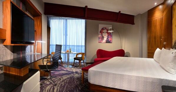 A hotel room with a bed, a TV, a desk with a chair, a table with chairs, and a window with curtains. - Hard Rock Hotel Guadalajara (Zapopan)