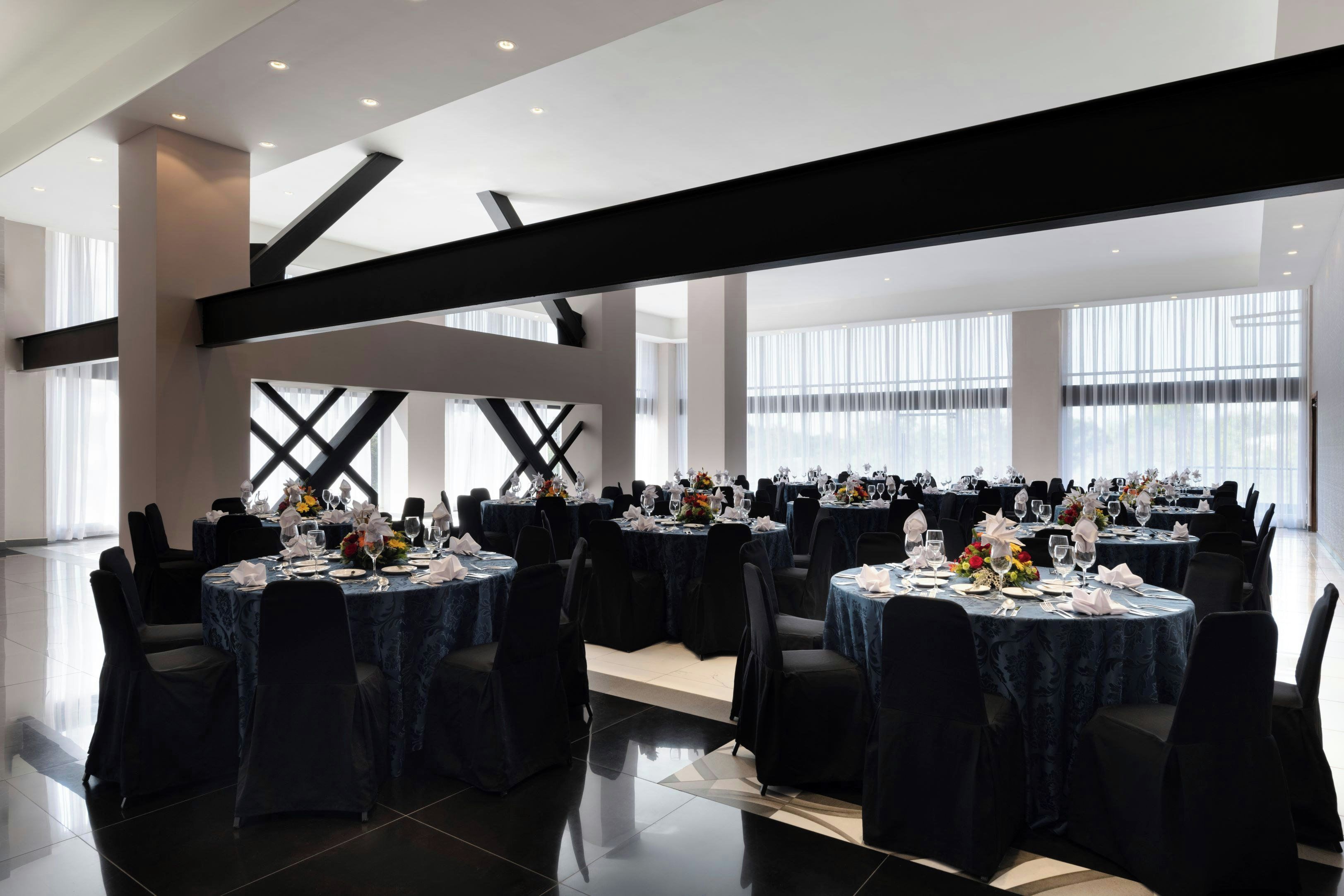 Un amplio salón de banquetes con varias mesas redondas, cada una con vajilla blanca y centros de mesa florales.