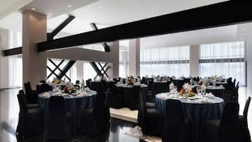 Un amplio salón de banquetes con varias mesas redondas, cada una con vajilla blanca y centros de mesa florales.