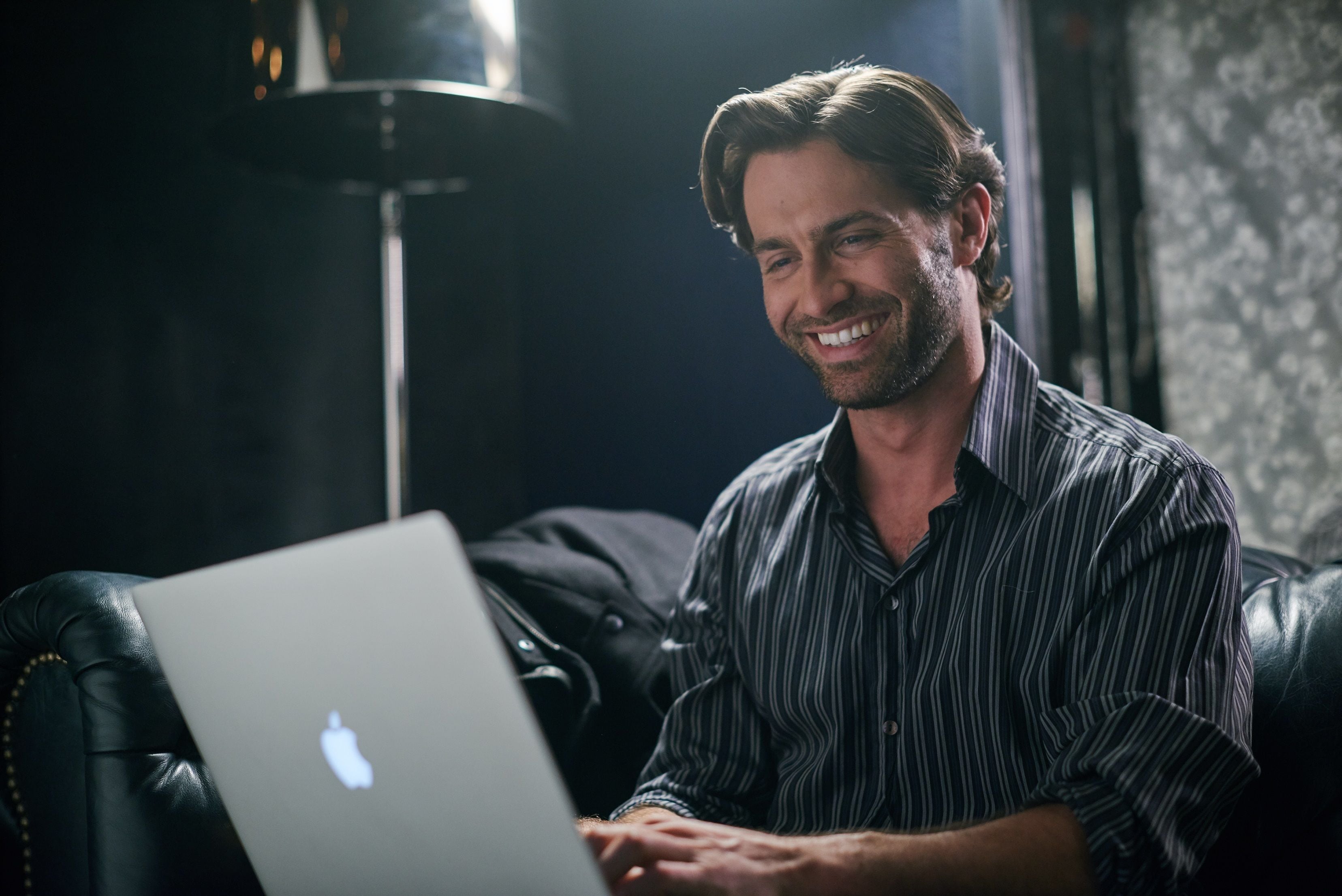 A person sitting on a leather couch with a laptop.