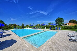 A pool area with two rectangular pools, surrounded by lounge chairs and umbrellas, under a clear blue sky.