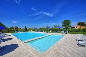 A pool area with two rectangular pools, surrounded by lounge chairs and umbrellas, under a clear blue sky.