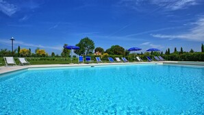 Una piscina con lettini e ombrelloni, immersa nel verde e alberi.