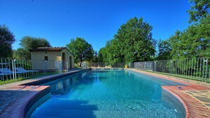 Ein klarer Pool mit Ziegelrand, umgeben von einem Metallzaun, und ein Gebäude mit einem geziegelten Dach im Hintergrund.