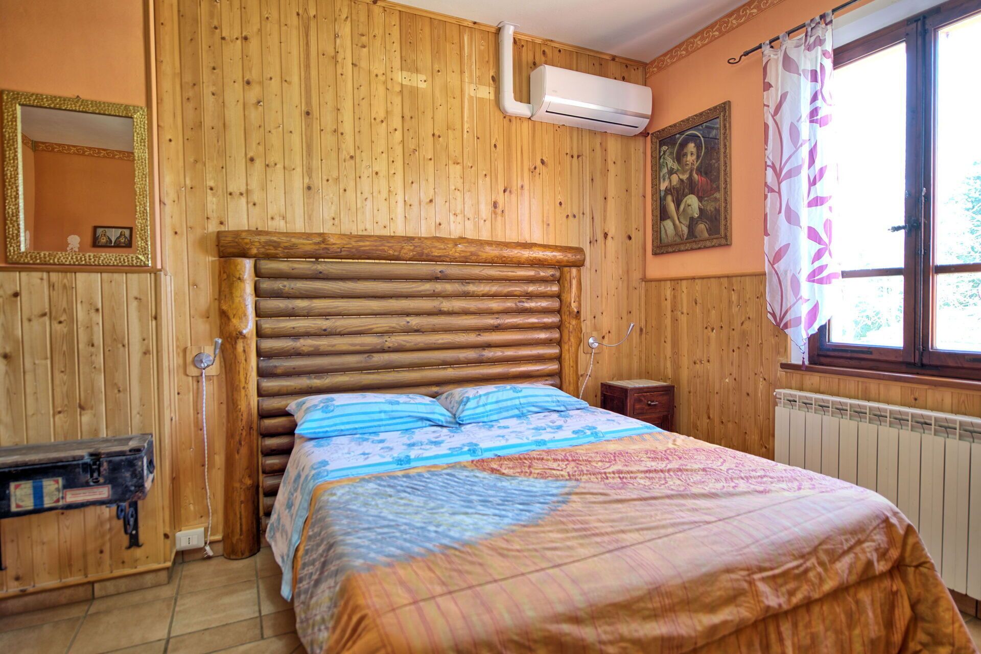 A wooden-paneled room with a bed, a radiator, and a window with curtains.