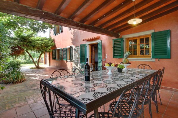 An outdoor patio with a table set for dining, surrounded by chairs.