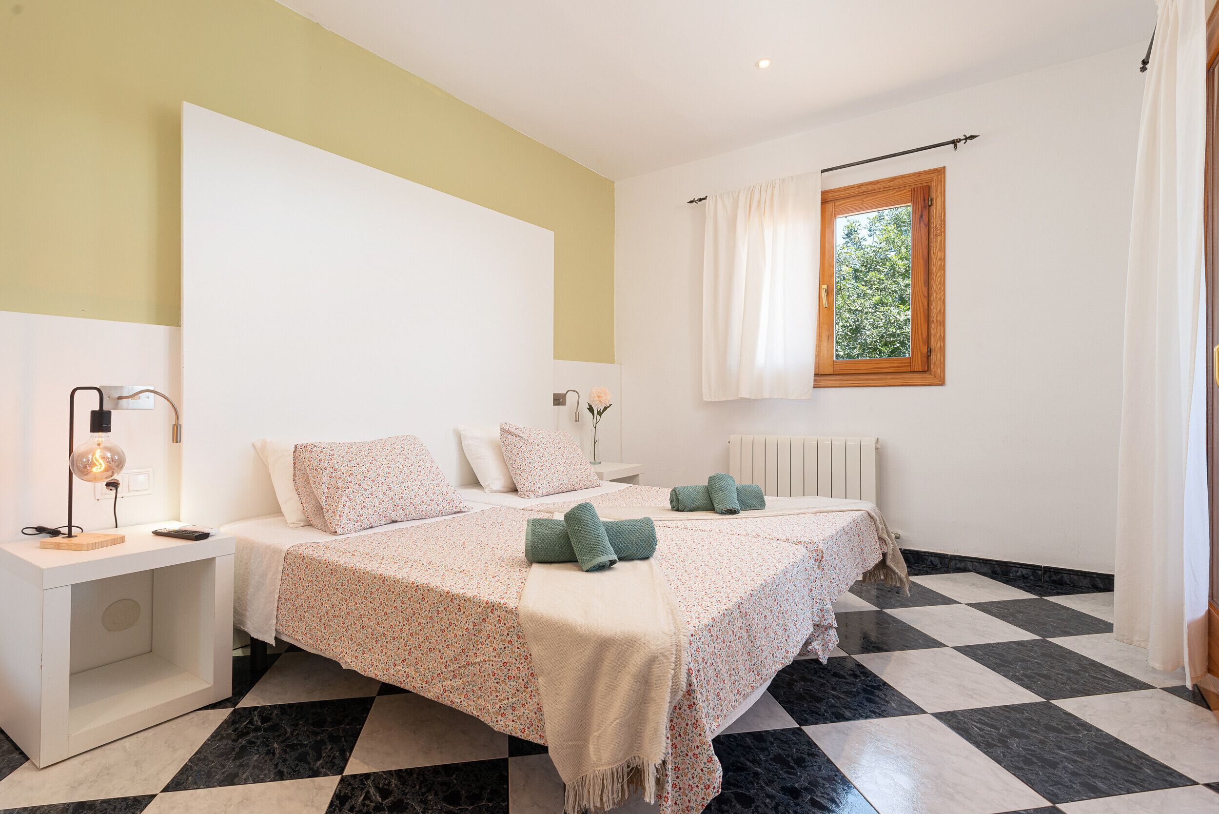 Un dormitorio con dos camas, una mesita de noche, una lámpara y una ventana con cortinas.