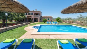 Una piscina con lettini, un edificio con un balcone e un cielo sereno.