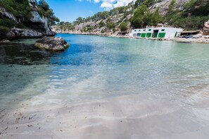 Paesaggio costiero con acque limpide, spiaggia sabbiosa e un edificio con porte verdi.
