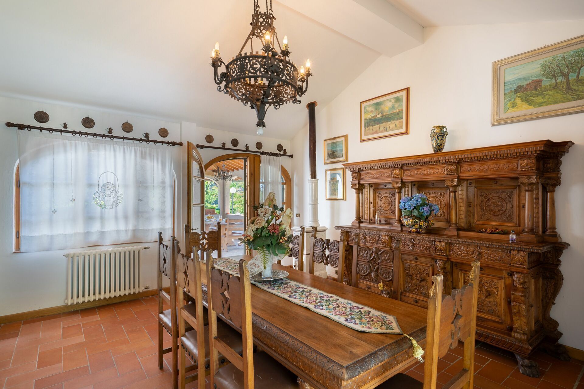 Comedor con mesa de madera, sillas, una araña y un aparador de madera con detalles tallados.