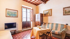 A room with a television, a table set with a bowl and glasses, a patterned sofa, and a cabinet. - Wonderful private villa for 16 people with private pool, WIFI, TV, patio and panoramic view (Vicchio)