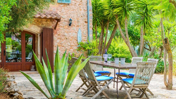 An outdoor patio with a stone table and chairs, surrounded by greenery and a rustic building. - CAN PINA - ECO PINA - Apartment with shared pool in Costitx. Free WiFi (Costitx)