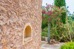A stone wall with a small arched window and a cactus garden with pink flowers. - CAN PINA - ECO PINA - Apartment with shared pool in Costitx. Free WiFi (Costitx)