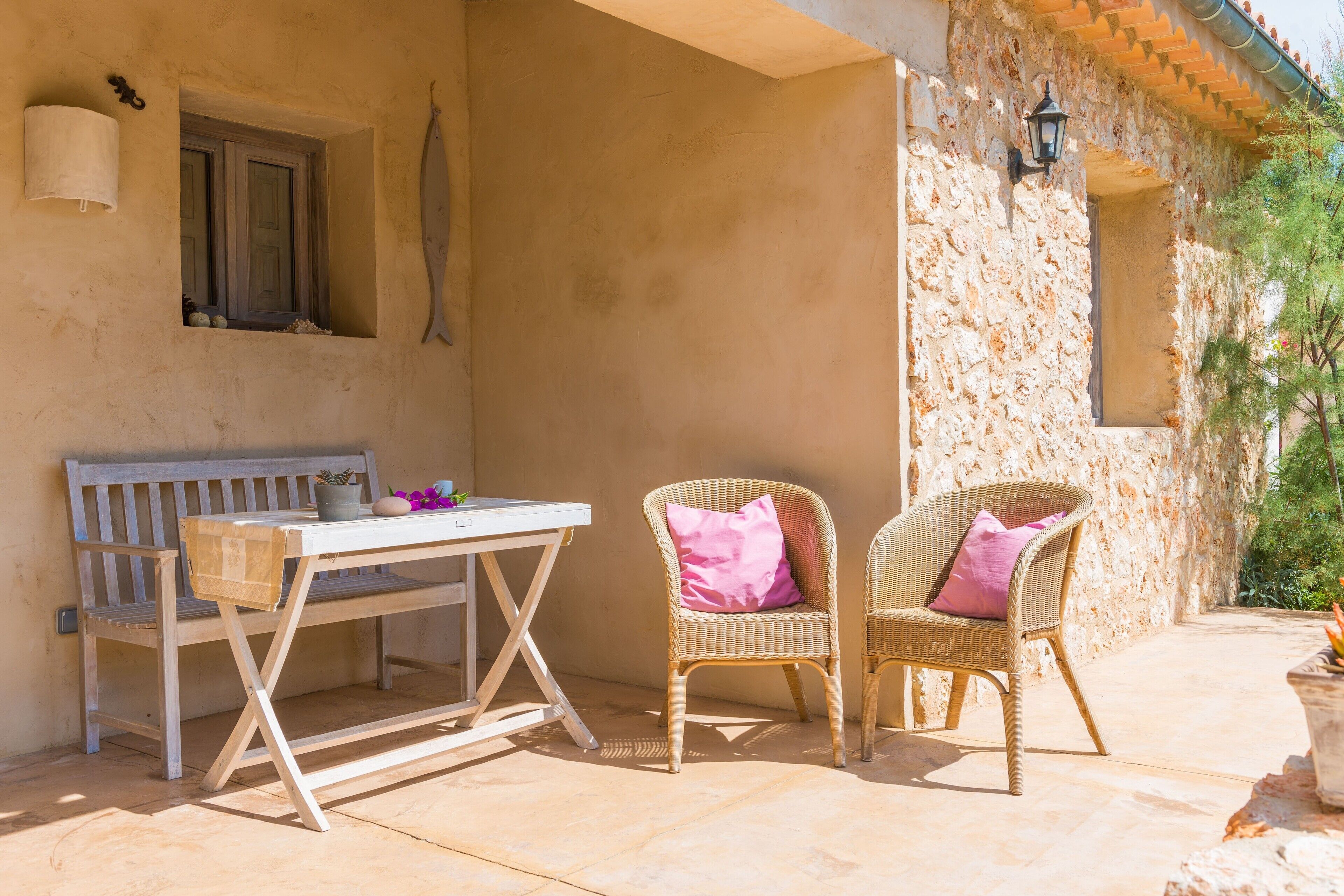Un espace extérieur aménagé avec une table et deux chaises en osier, dont l’une est agrémentée d’un coussin rose.