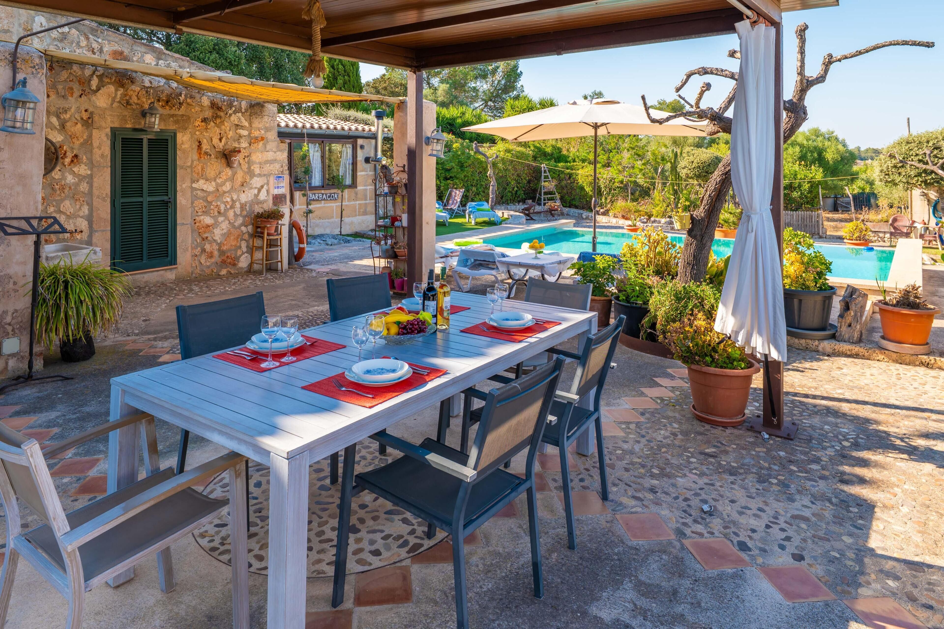 An outdoor dining area with a stone wall, a pool, and potted plants.