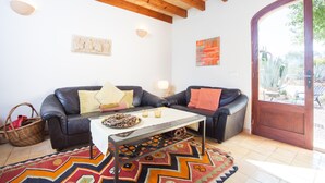 Sala de estar com sofá de couro preto, mesa de centro branca, tapete estampado e teto de madeira.