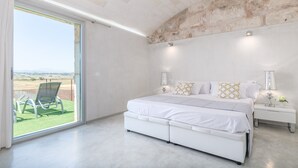 Ein Schlafzimmer mit einem großen Bett, einem Nachttisch, einer Lampe und Blick ins Freie durch eine Schiebetür.