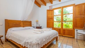 A bedroom with a wooden bed, white linens, a nightstand with a lamp, and a view through a large window. - SES PLANES (CA NA FAUSTINA) - Villa with private pool in SELVA. Free WiFi (Selva)