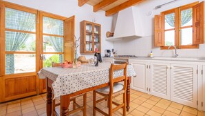 A kitchen with wooden cabinets, a dining table with a polka dot tablecloth, and a window with wooden shutters. - SES PLANES (CA NA FAUSTINA) - Villa with private pool in SELVA. Free WiFi (Selva)