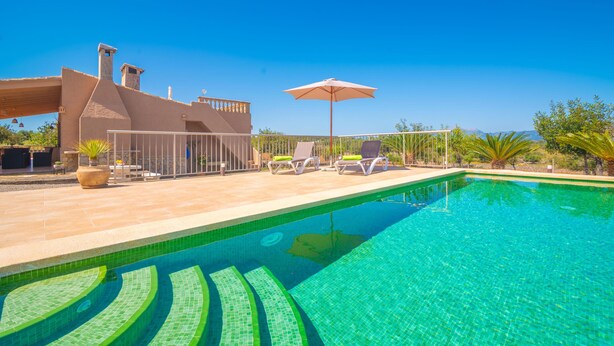 Una piscina con acqua cristallina, una zona patio coperta con poltrone relax e un edificio con tetto a falda.