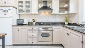 A modern kitchen with white cabinets, a stainless steel range hood, a built-in oven, and a microwave.