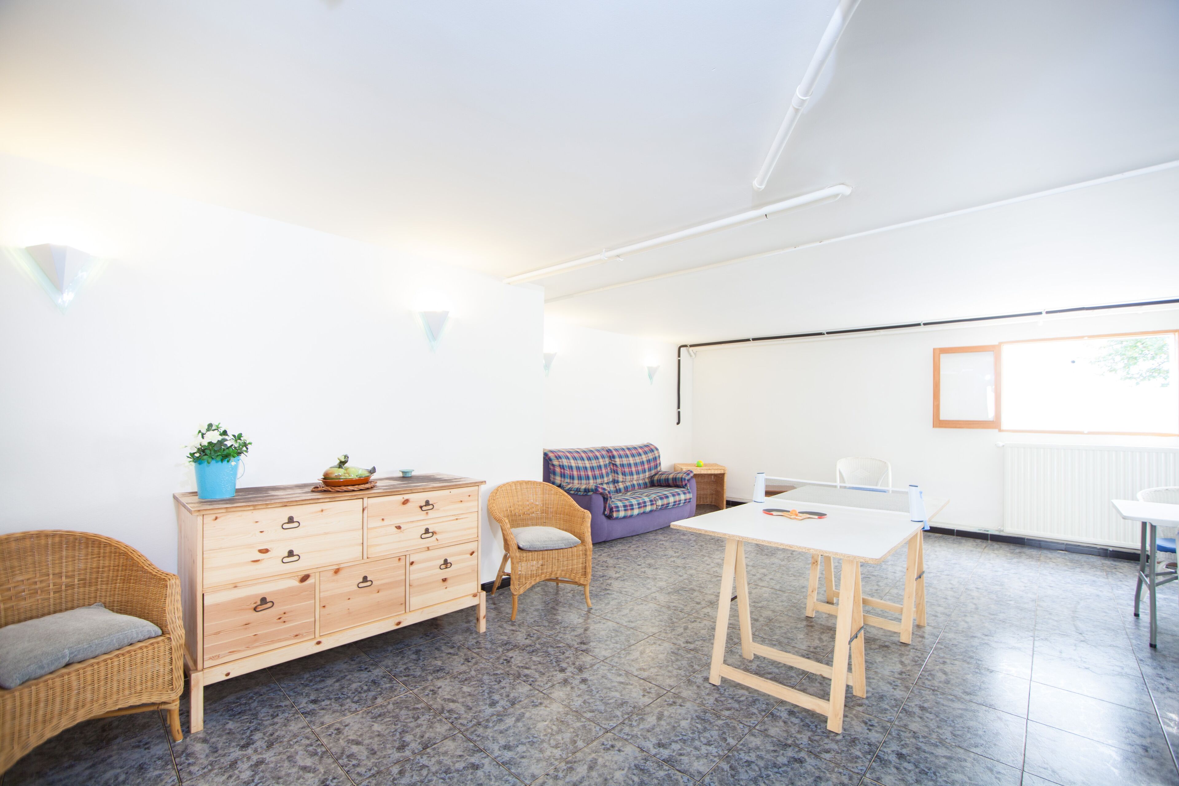 Una habitación luminosa y amplia con un aparador de madera, muebles de mimbre, un sofá morado y una mesa blanca.