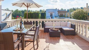 A terrace with a dining table, chairs, a sofa, and an umbrella.