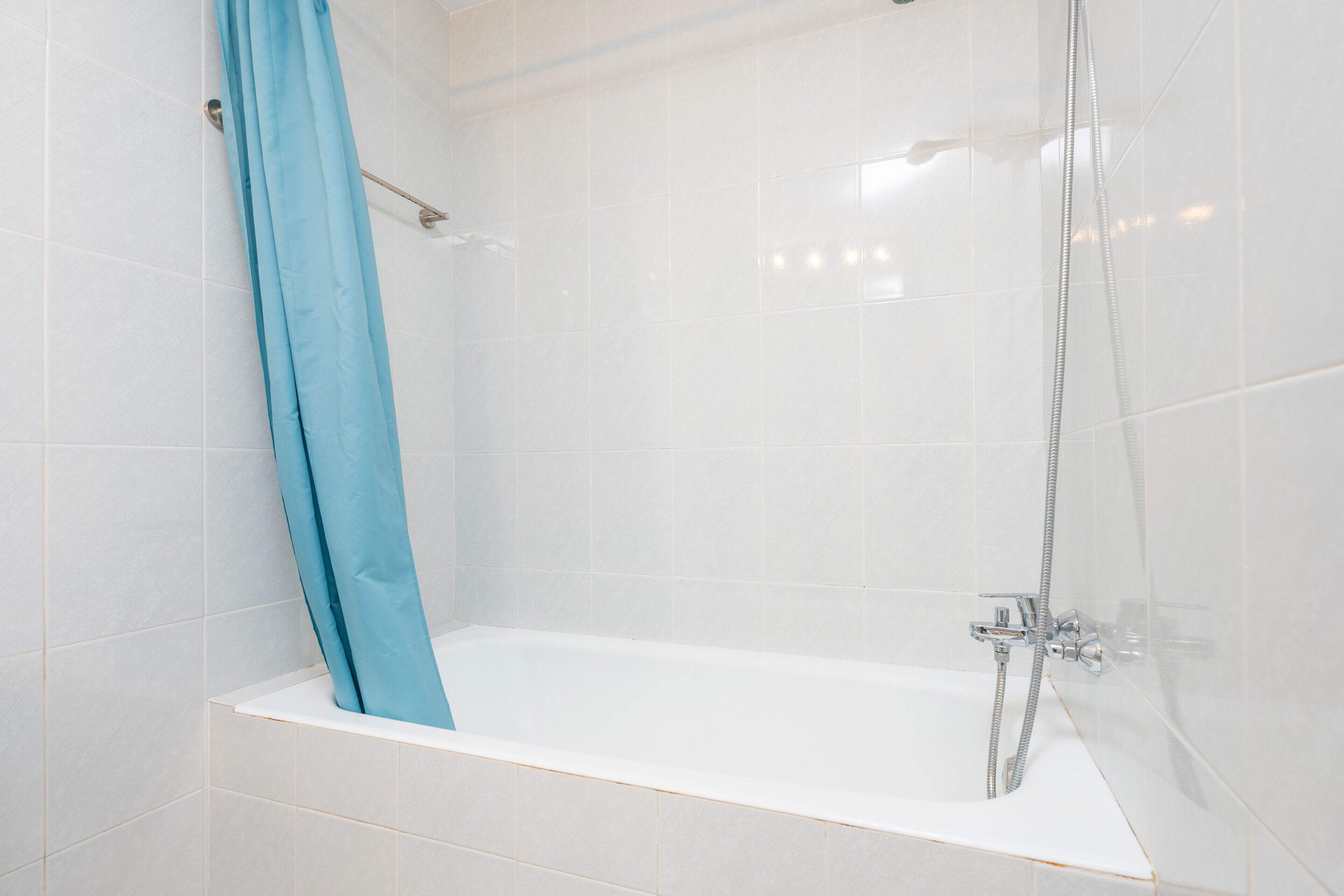 Een moderne badkamer met witte tegels, een badkuip en een douche met een chromen kraan.