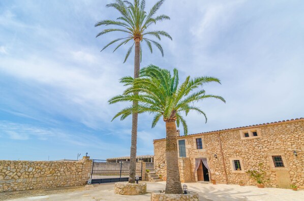 A stone building with a tiled roof, palm trees, and a gated entrance.