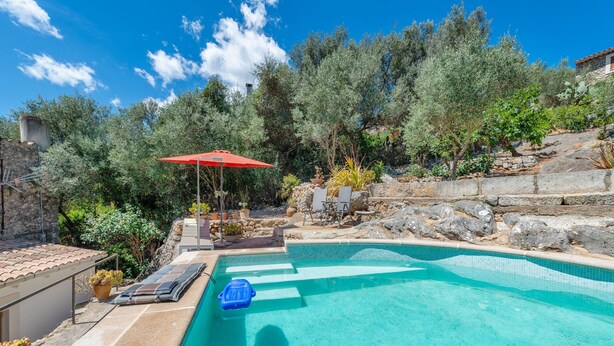 A swimming pool with a red umbrella, lounge chairs, and potted plants.