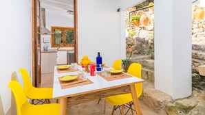 A dining area with a white table set for four, yellow chairs, and a stone wall with potted plants.