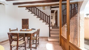 A dining area with a wooden table and chairs, a staircase with wooden railings, and a view through a glass door.