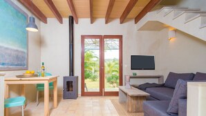 Ein Wohnzimmer mit einer Couch, einem Fernseher, einem Kamin, einem Esstisch mit Stühlen und einem großen Fenster mit Blick auf Grünflächen.
