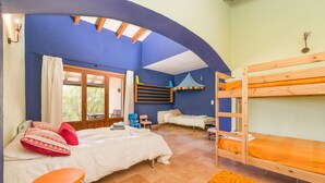 Une pièce comprenant deux lits superposés, un lit simple, une chaise en bois, une petite table et une fenêtre avec des rideaux.