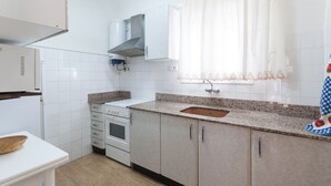 A kitchen with white cabinets, a granite countertop, a stainless steel sink, and a window with white curtains. - ODISEA - Apartment with sea views in Playa de Piles. (Playa de Piles)