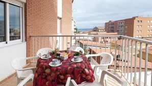 A balcony with a table set for two, white plastic chairs, and a red tablecloth with apple prints. - ODISEA - Apartment with sea views in Playa de Piles. (Playa de Piles)
