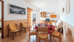 A dining area with a table set for four, surrounded by four chairs with floral upholstery. There is a television on a wooden cabinet, and a painting is visible on the wall. - ODISEA - Apartment with sea views in Playa de Piles. (Playa de Piles)