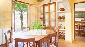 Un coin repas avec une table en bois, des chaises et une plante en pot. Il y a une fenêtre donnant sur un arbre et une porte menant à une autre pièce.
