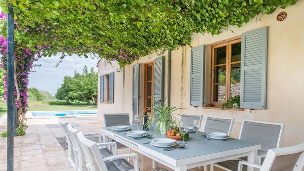 Un espace de restauration en plein air avec une table dressée pour six personnes, entourée de chaises blanches dotées de coussins gris.