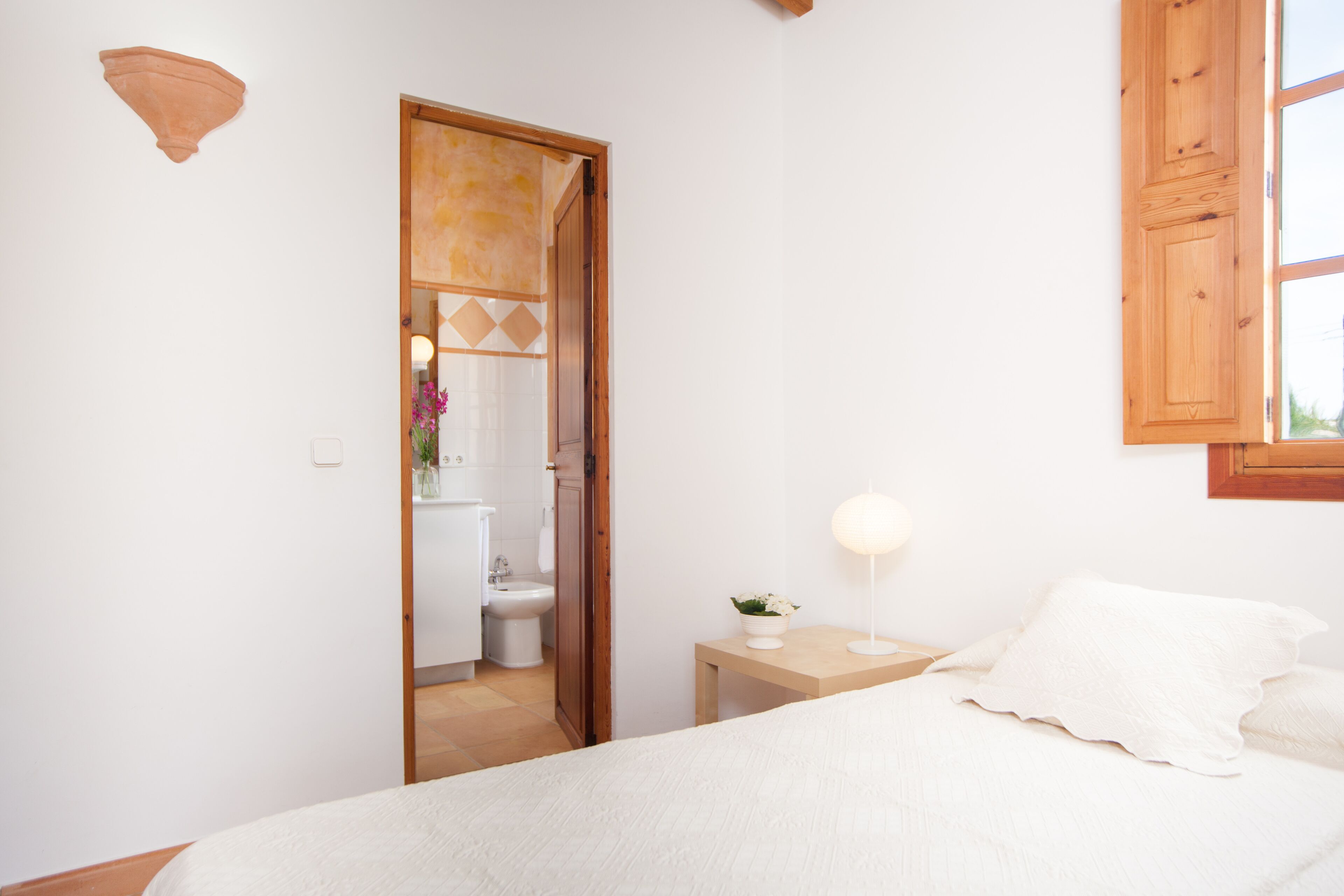 A bedroom with a bed, bedside table, and a view of the bathroom.