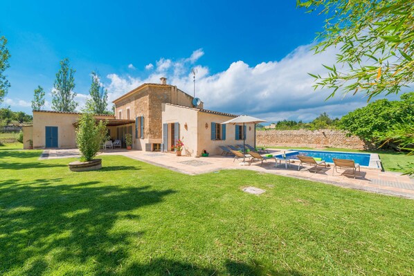 A two-story house with a swimming pool, a patio with chairs, and a well-maintained lawn.