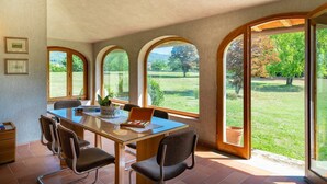 A dining area with a glass table, four chairs, and large arched windows offering a view of a grassy landscape. - Villa in Vicchio with 4 bedrooms sleeps 8 (Vicchio)