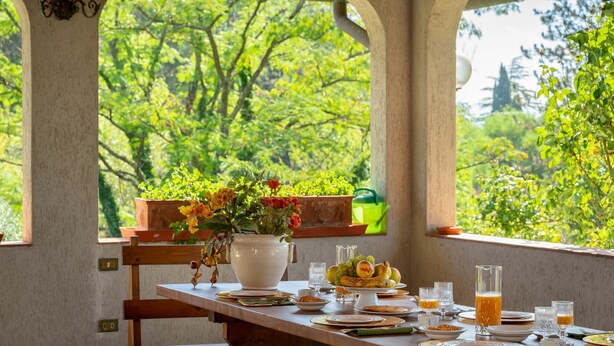 A dining table set with plates, glasses, and a fruit bowl, with a view of lush greenery through large windows. - Villa in Vicchio with 4 bedrooms sleeps 8 (Vicchio)