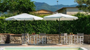 Ein Poolbereich mit zwei Sonnenschirmen, Steinmauern und Blick auf die Berge.