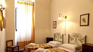 Ein Zimmer mit zwei Betten, einem Sessel, einer Lampe und einem Fenster mit Vorhängen.