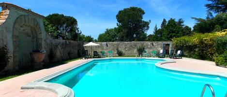A rectangular swimming pool with a stone wall and a tiled deck.
