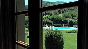 A view through a window of a swimming pool surrounded by lush greenery and hills.
